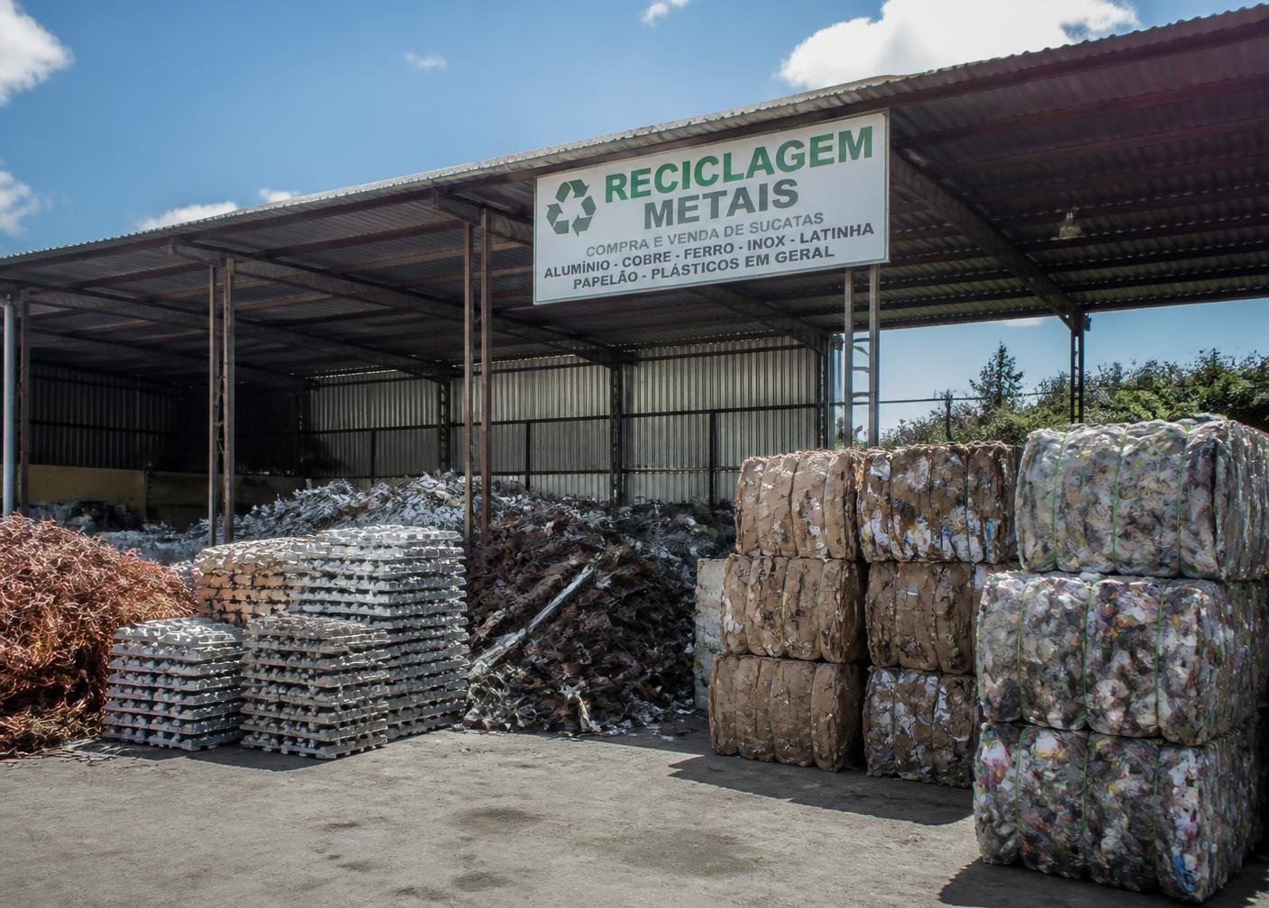Sucatas de cobre, alumínio e fardos de recicláveis organizados no galpão